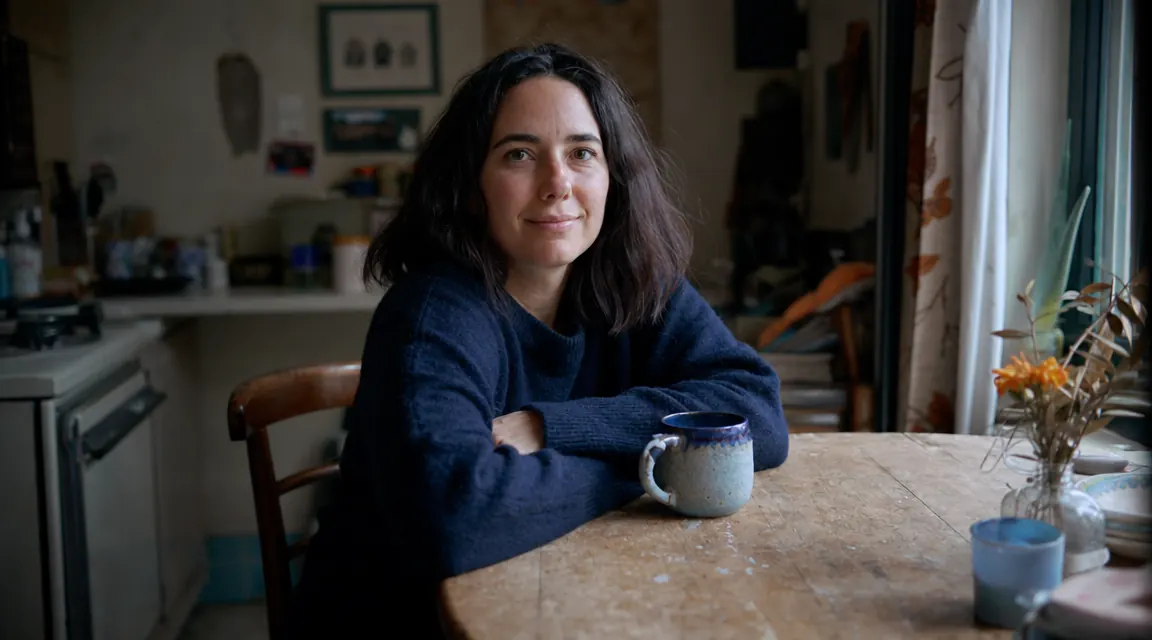 Person sitting at a kitchen table with a mug of coffee, relaxed morning light, looking rested, no phone in hand